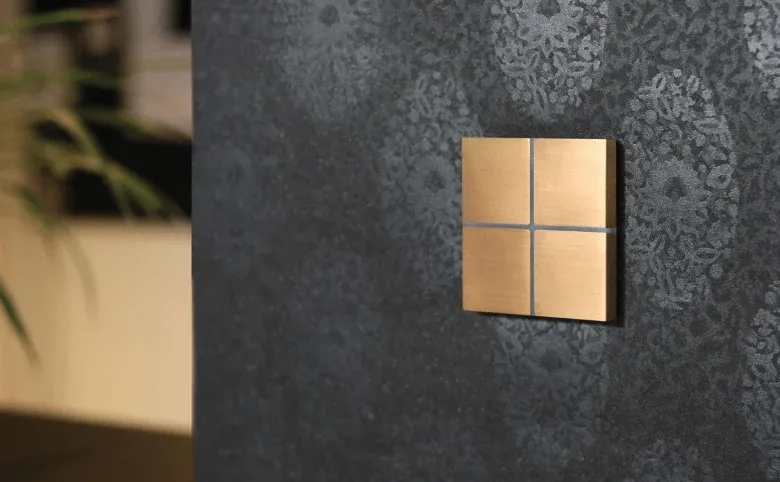 A brass KNX push-button on a textured wall